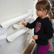Child placing a ball on a white magnetic wall panel with ramps and cups, framed by durable Wormy Maple wood trim.