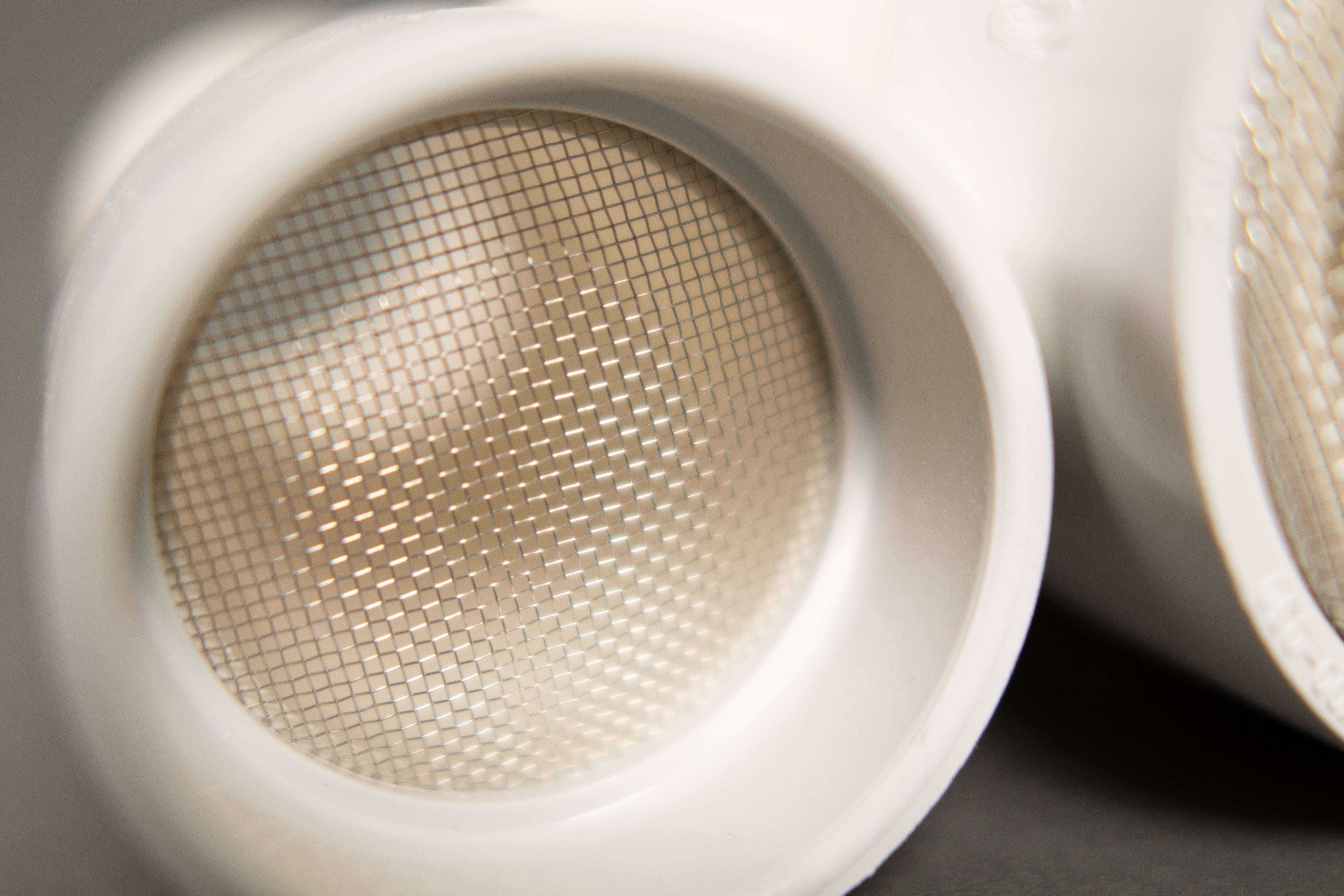 Close-up of white plastic Jurassic Sifter Scoops featuring a fine metal mesh screen for filtering sand.