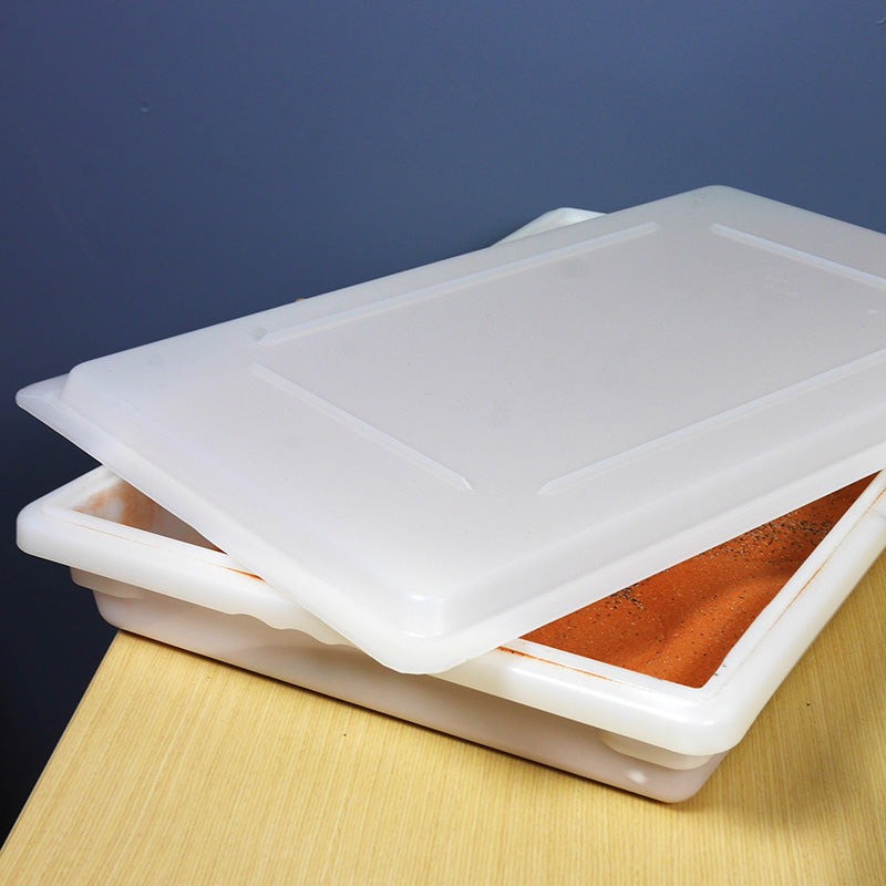 White rectangular sensory bin with a matching lid, partially filled with fine orange Jurassic play sand.
