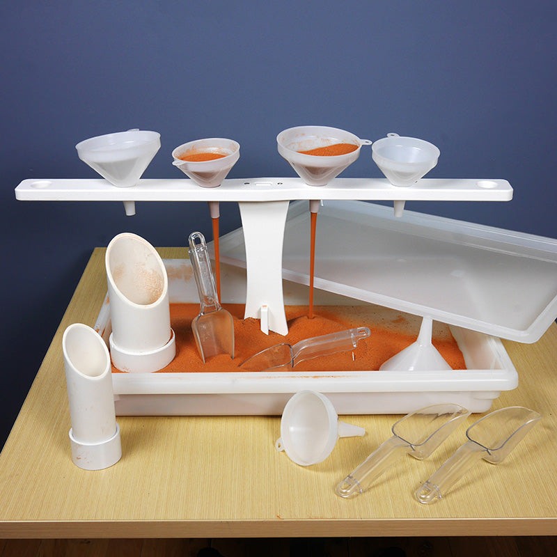 Kodo sand and water kit with a white funnel stand, clear scoops, and orange Jurassic sand in a sensory bin on a table.