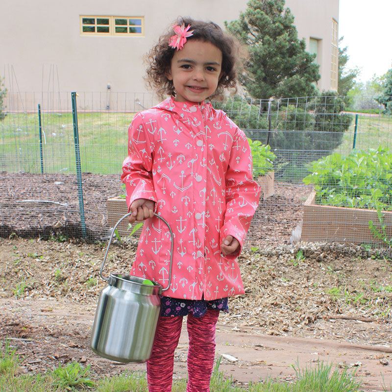 Young girl in a pink anchor raincoat holding a durable stainless steel bucket for sand and water play.