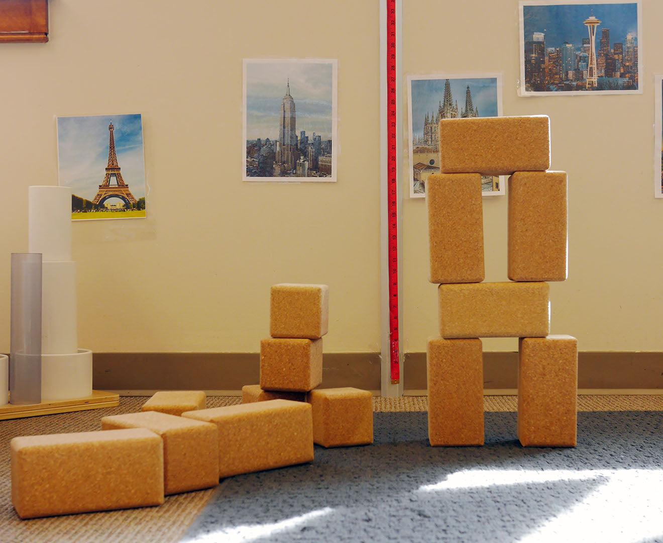 Large, natural cork building blocks stacked into towers and rectangles on a blue carpeted floor.