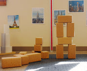 Large, natural cork building blocks stacked into towers and rectangles on a blue carpeted floor.