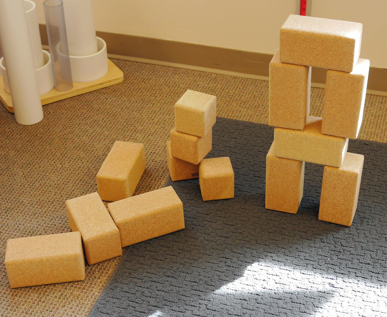 Large, natural cork building blocks in rectangular and cube shapes stacked into a tower on a grey mat.