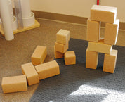Large, natural cork building blocks in rectangular and cube shapes stacked into a tower on a grey mat.