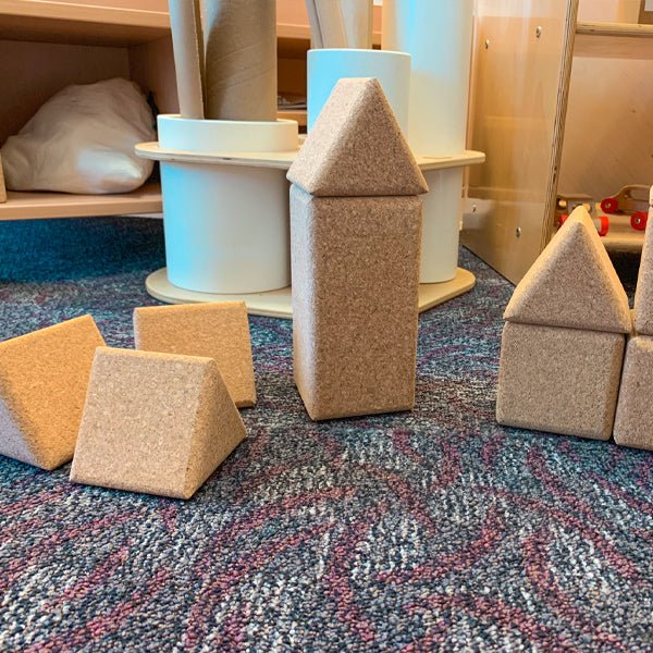 Large, natural cork triangle and rectangular building blocks arranged on a colorful patterned carpet.