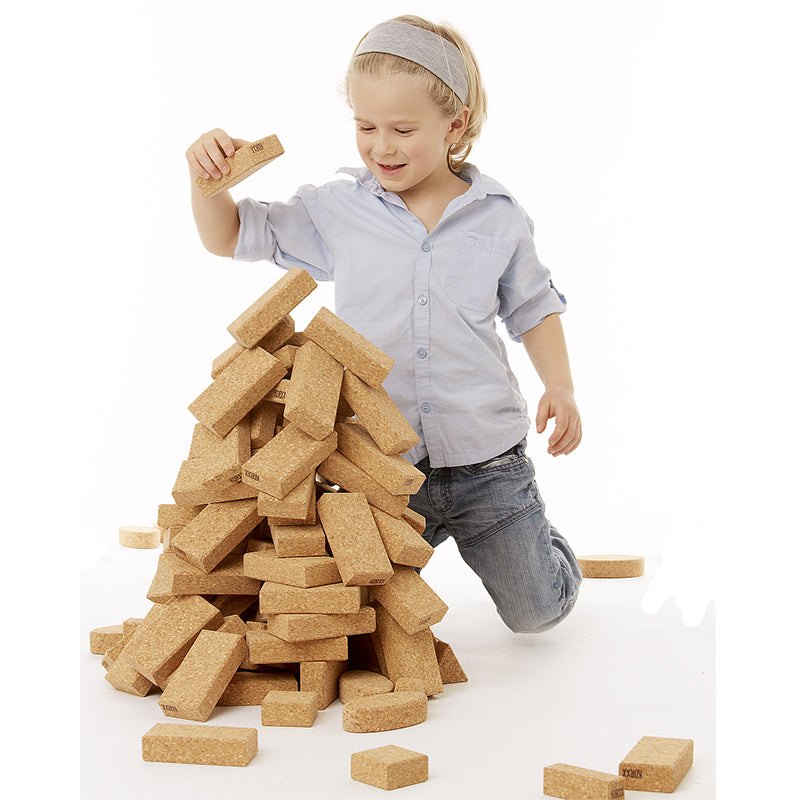 Child building a tall tower with lightweight, natural cork building blocks on a white background.