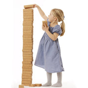 Young girl stacking lightweight, textured cork building blocks into a tall, stable tower against a white background.