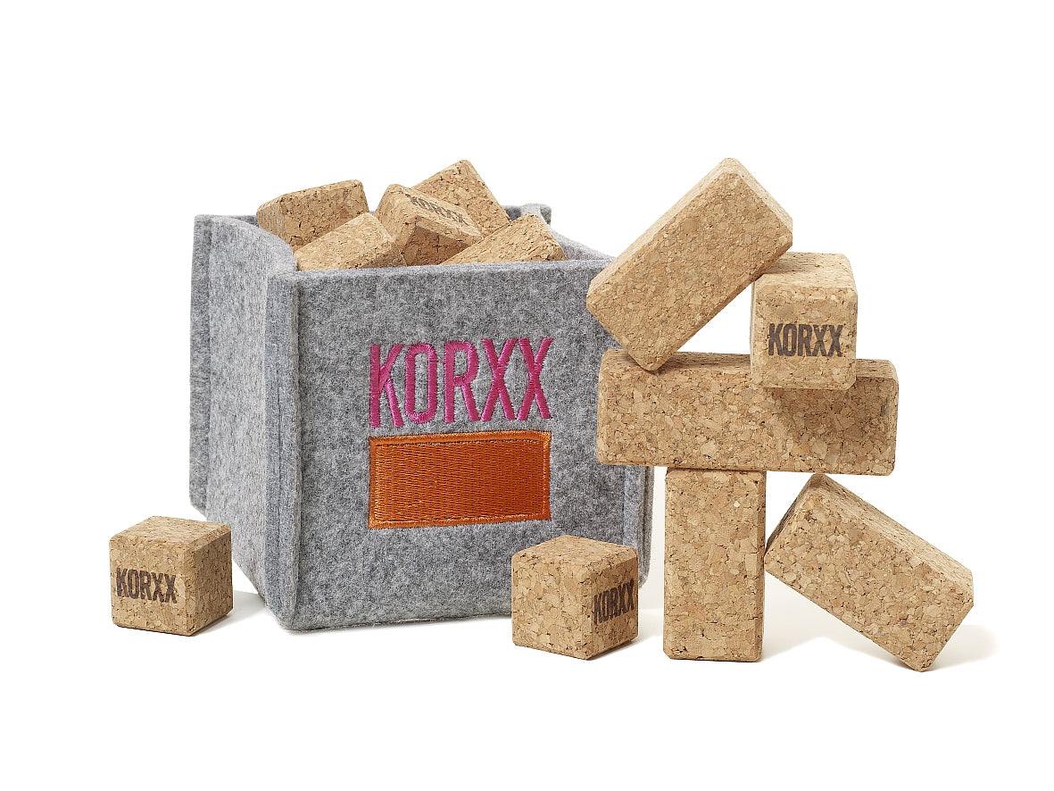 Natural cork building blocks in a grey felt storage bin with Korxx branding, isolated on a white background.