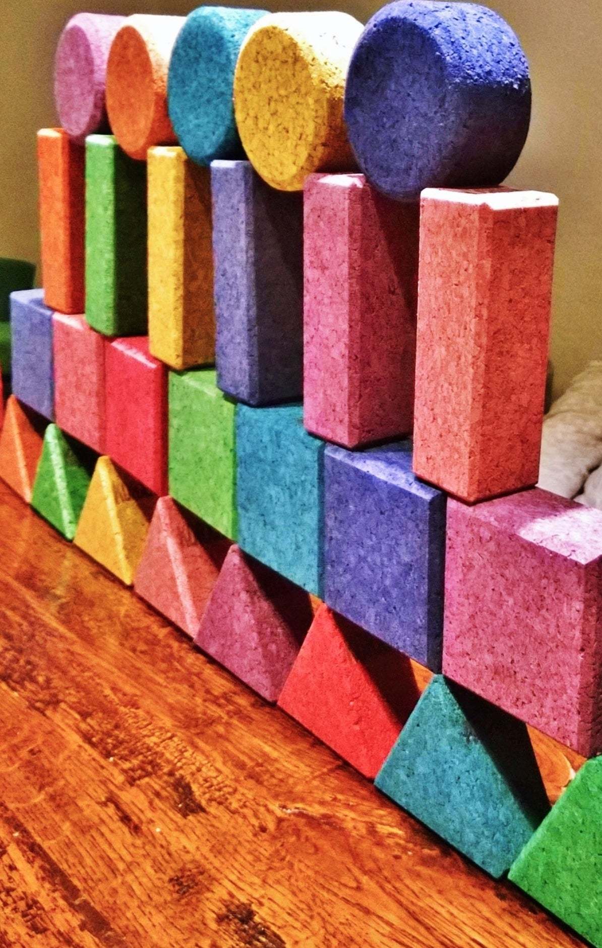 Set of 56 vibrant, multicolored cork building blocks in geometric shapes like circles, squares, and triangles on a wooden table.