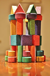 Vibrant, multi-colored cork building blocks in various geometric shapes stacked into a tall, stable tower structure.