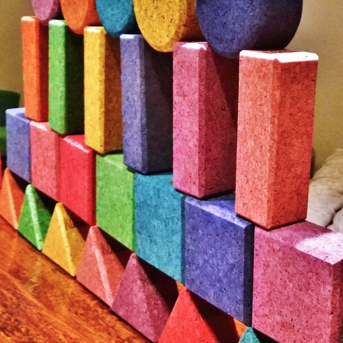 Colorful Korxx cork building blocks in various geometric shapes stacked on a wooden surface.