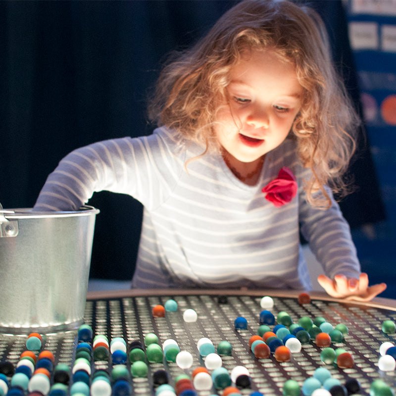 Child placing colorful frosted marbles on a glowing Light Lab board to explore light refraction and color theory.