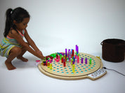 Child playing with a circular birch wood light-up pegboard and colorful translucent acrylic pegs.
