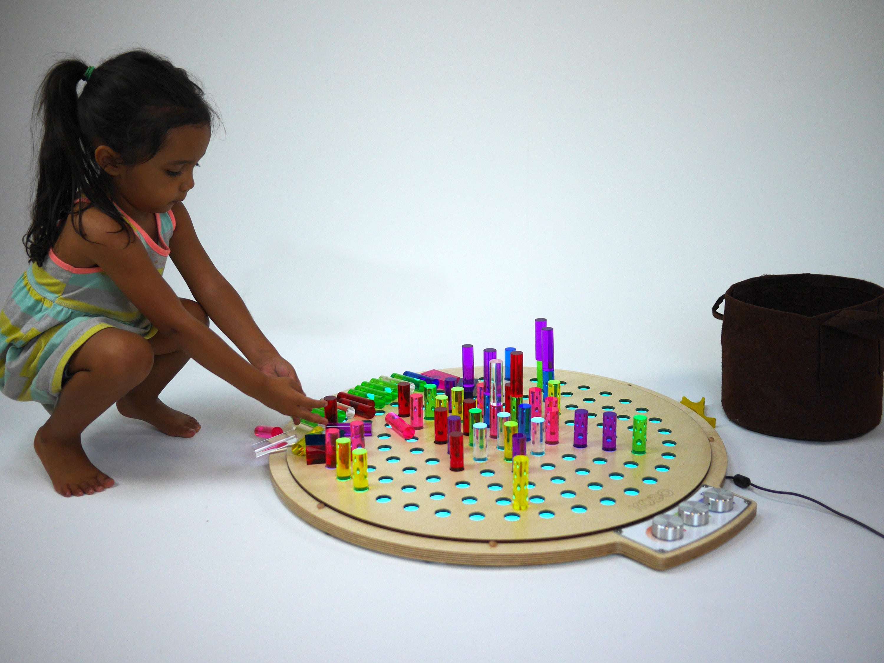 Child playing with a circular birch wood light-up pegboard and colorful translucent acrylic pegs.