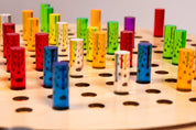 Vibrant rainbow-colored acrylic pegs inserted into a natural birch wooden pegboard with circular holes.