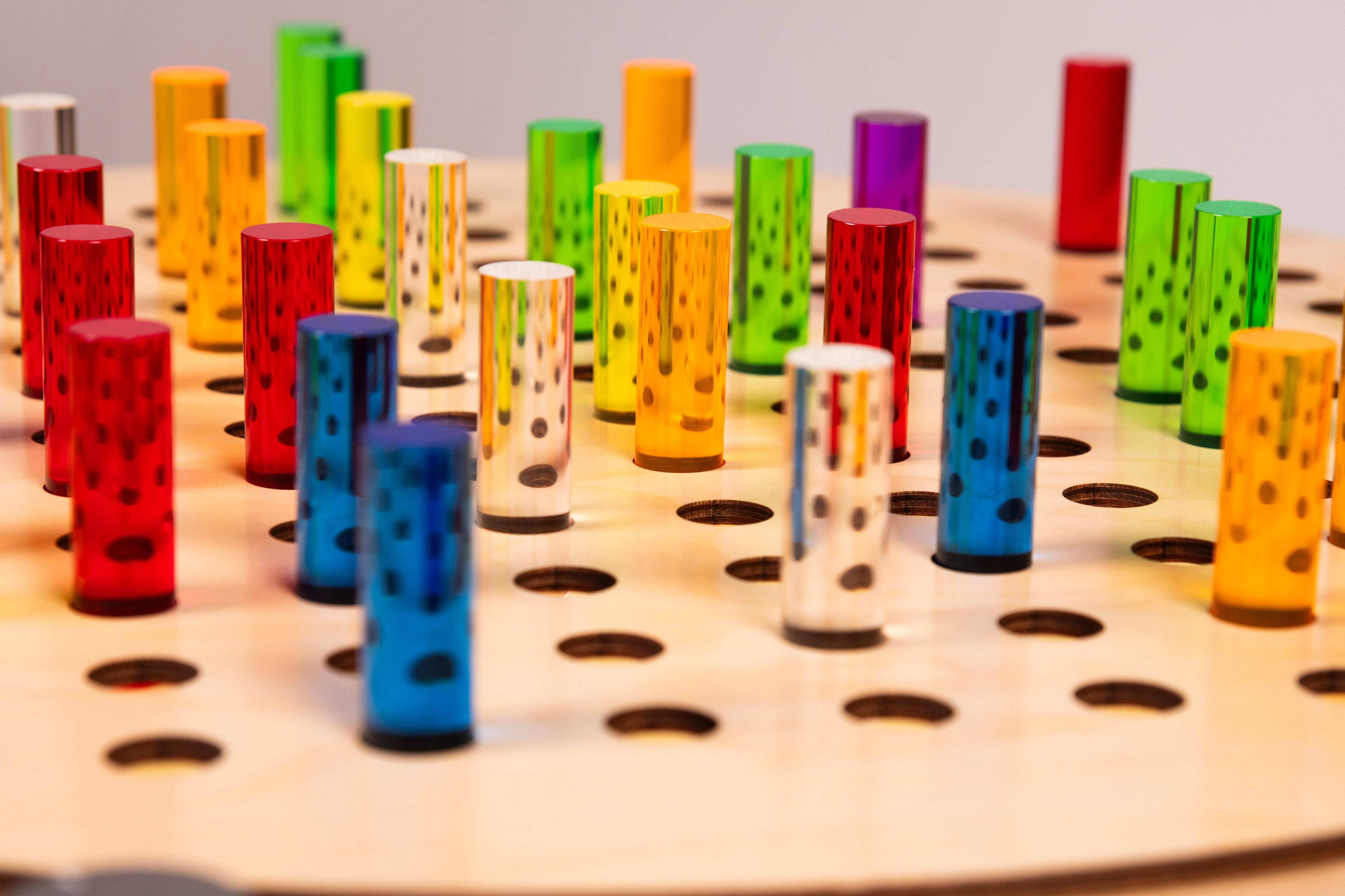Vibrant rainbow-colored acrylic pegs inserted into a natural birch wooden pegboard with circular holes.
