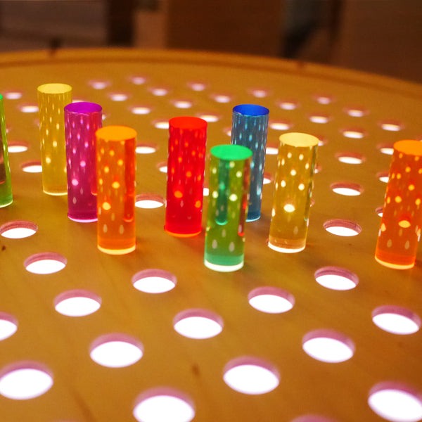 Vibrant acrylic pegs in rainbow colors standing on a light-up natural birch circular pegboard.