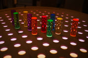 Vibrant acrylic pegs in rainbow colors arranged on a light-up birch grid pegboard for creative play.