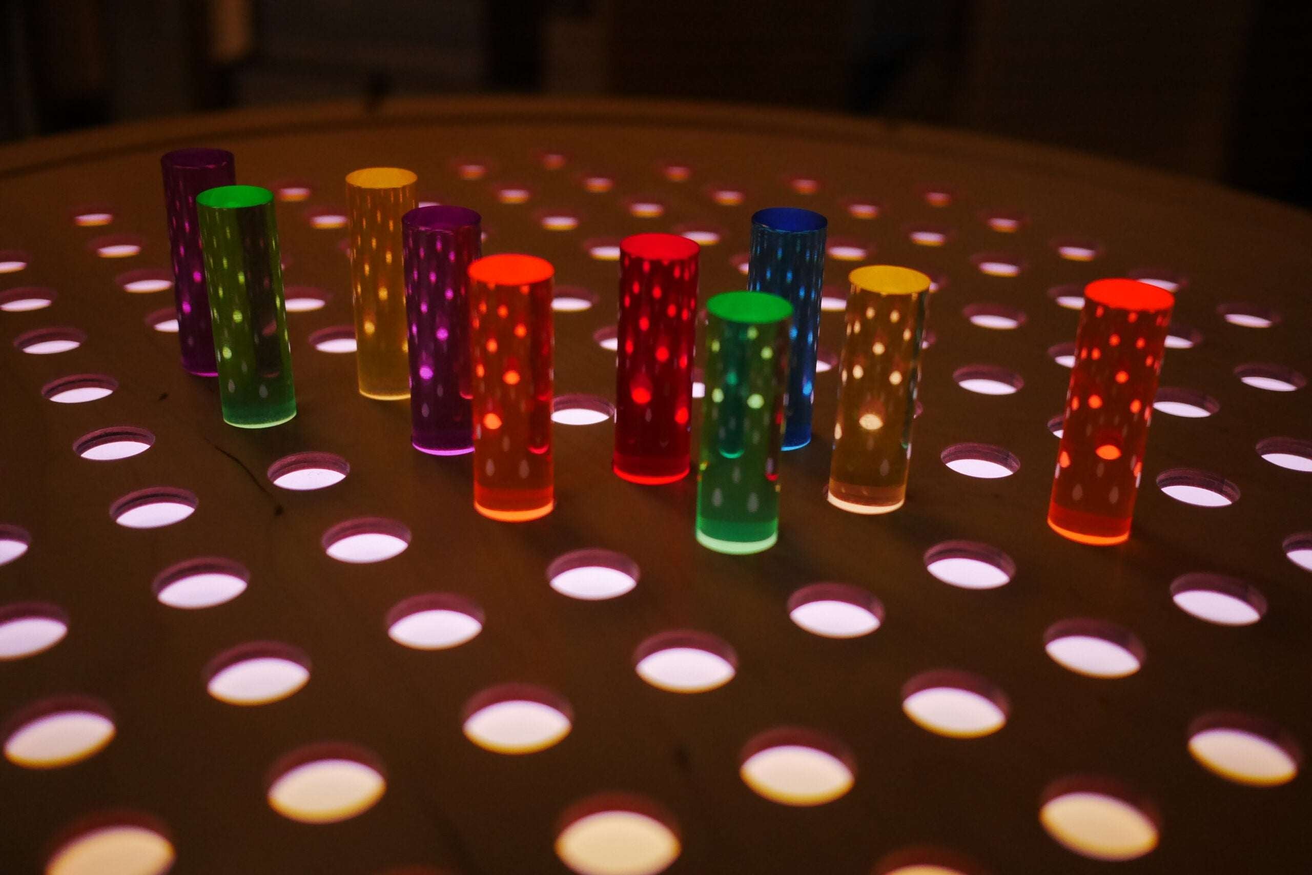 Vibrant acrylic pegs in rainbow colors arranged on a light-up birch grid pegboard for creative play.