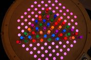 Circular birch pegboard with glowing, colorful acrylic pegs arranged in a grid pattern on a light table.
