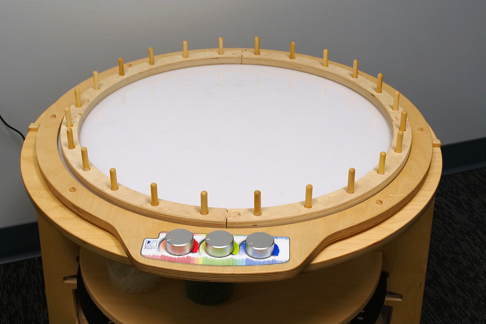 Four-piece wooden weaving ring with pegs, resting on a round light table with three colorful control knobs.