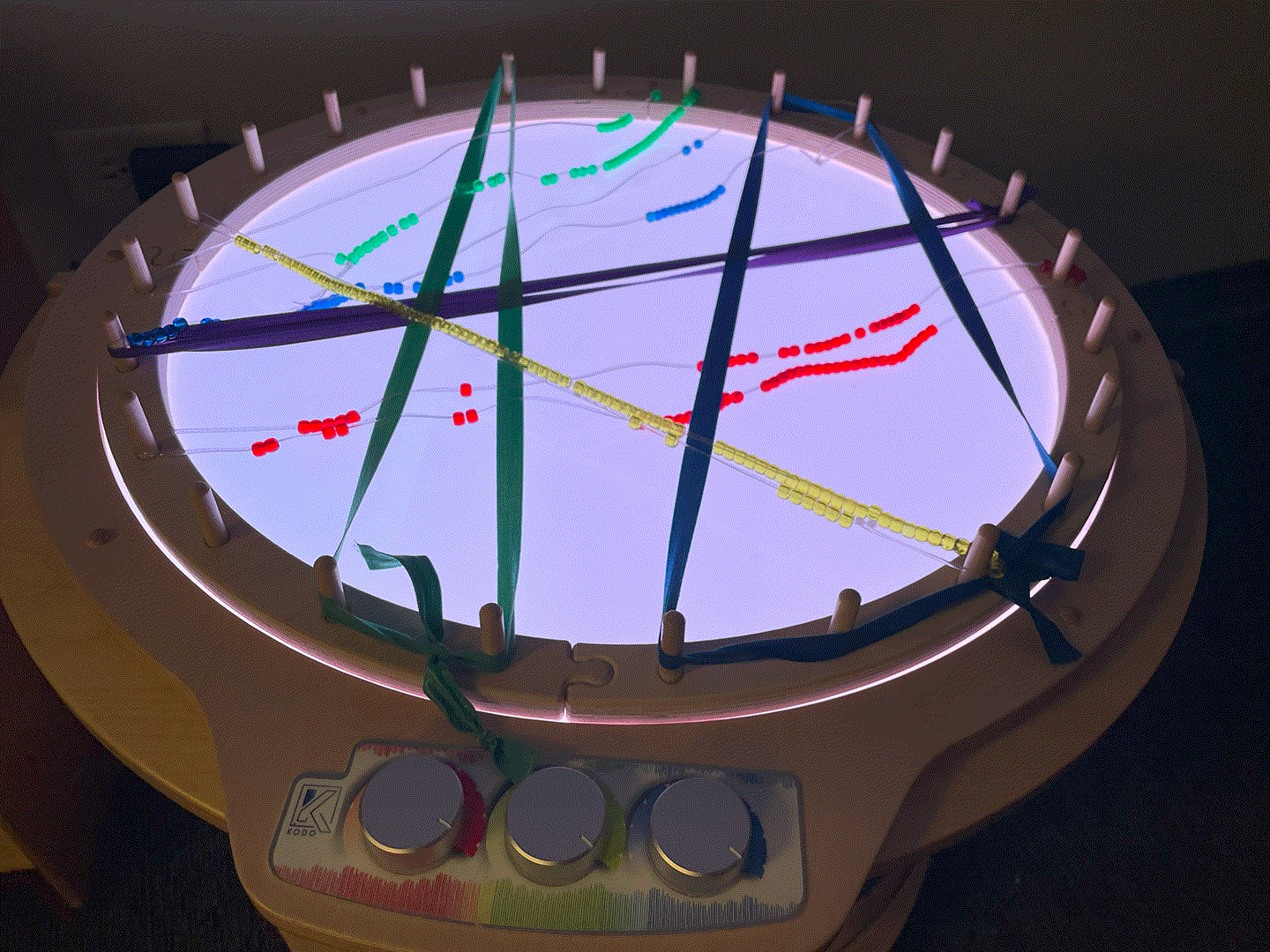 Light Lab Weaving Ring with colorful ribbons and beads strung across a circular, light-up wooden frame with puzzle edges.
