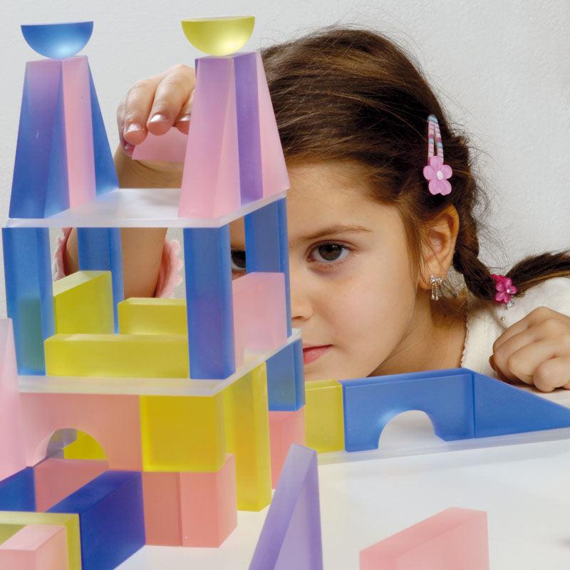 Child building with vibrant, frosted translucent blocks in various geometric shapes and soft pastel colors.