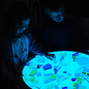 Children playing with colorful, frosted translucent building blocks on a glowing blue light table.