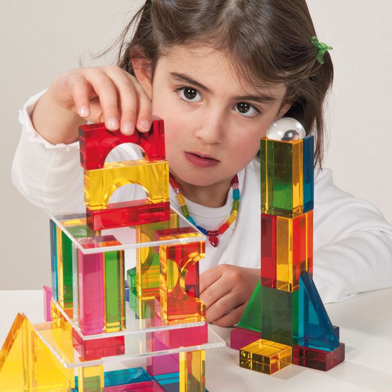 Child building with colorful, glossy, transparent Luxi blocks on a white surface.