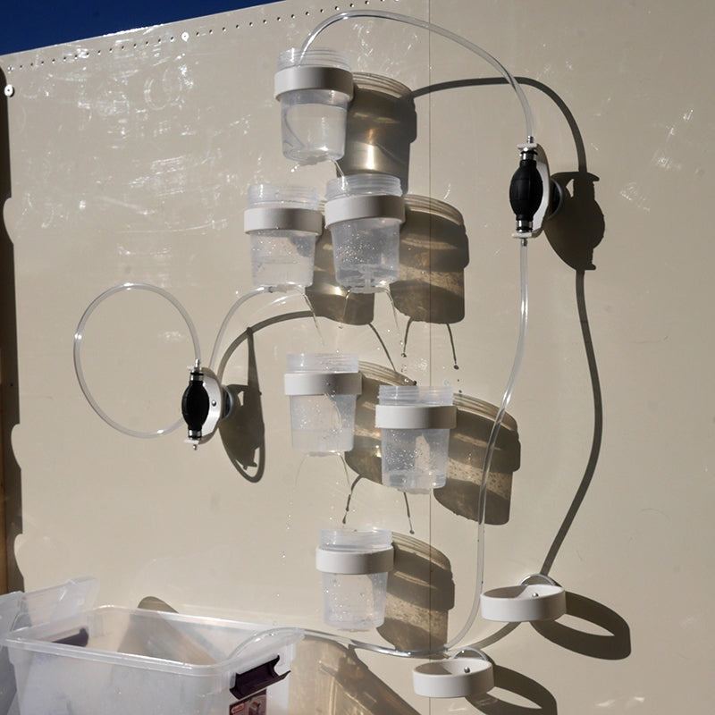 Modular water circuit with clear cups, tubing, and black hand pumps mounted on a magnetic wall for STEM play.
