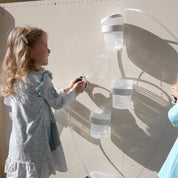 Child playing with a magnetic water circuit set featuring clear tubes and containers on a vertical wall.