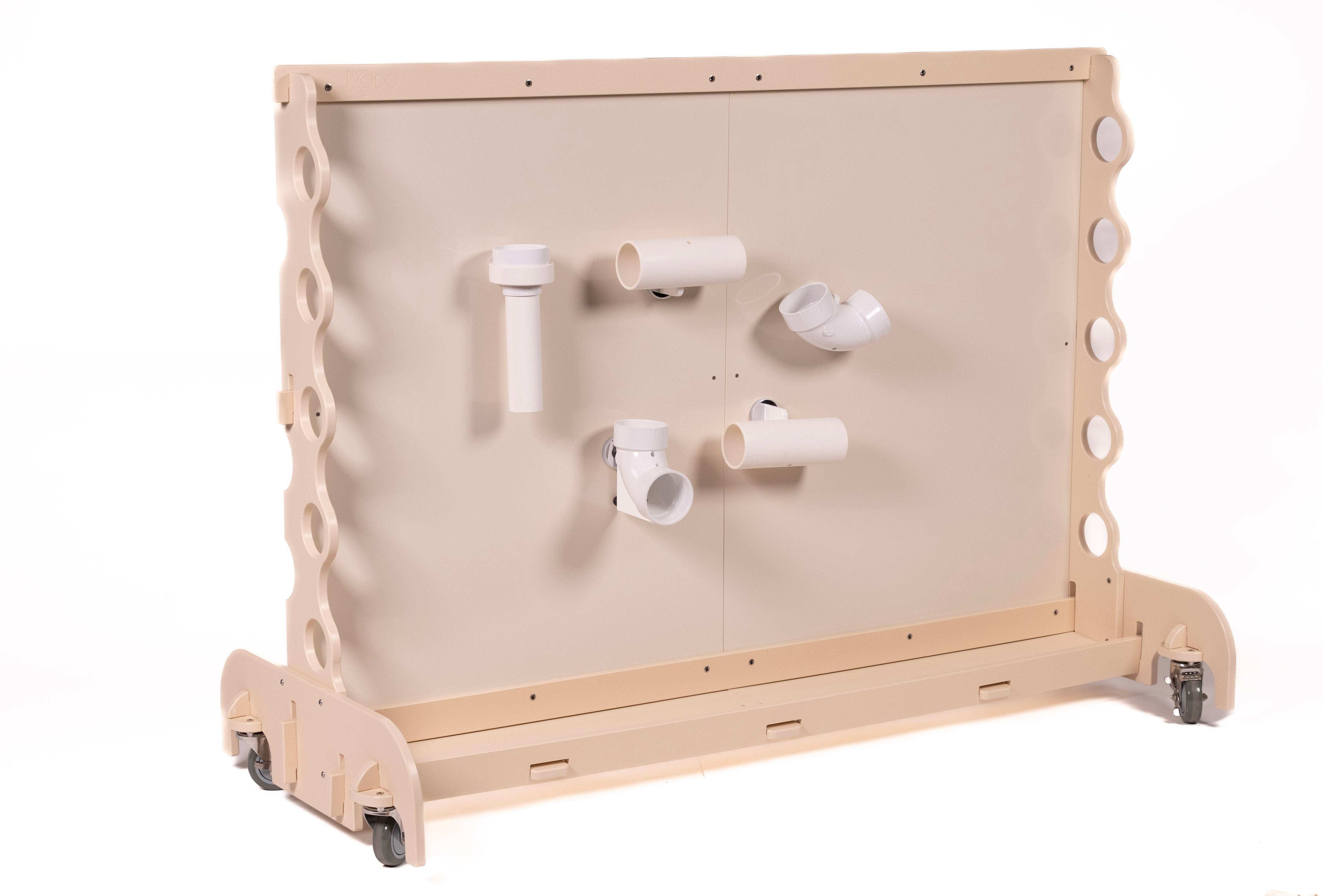 Light wood mobile magnet wall featuring various white PVC chutes and tubes attached to the smooth central panel.