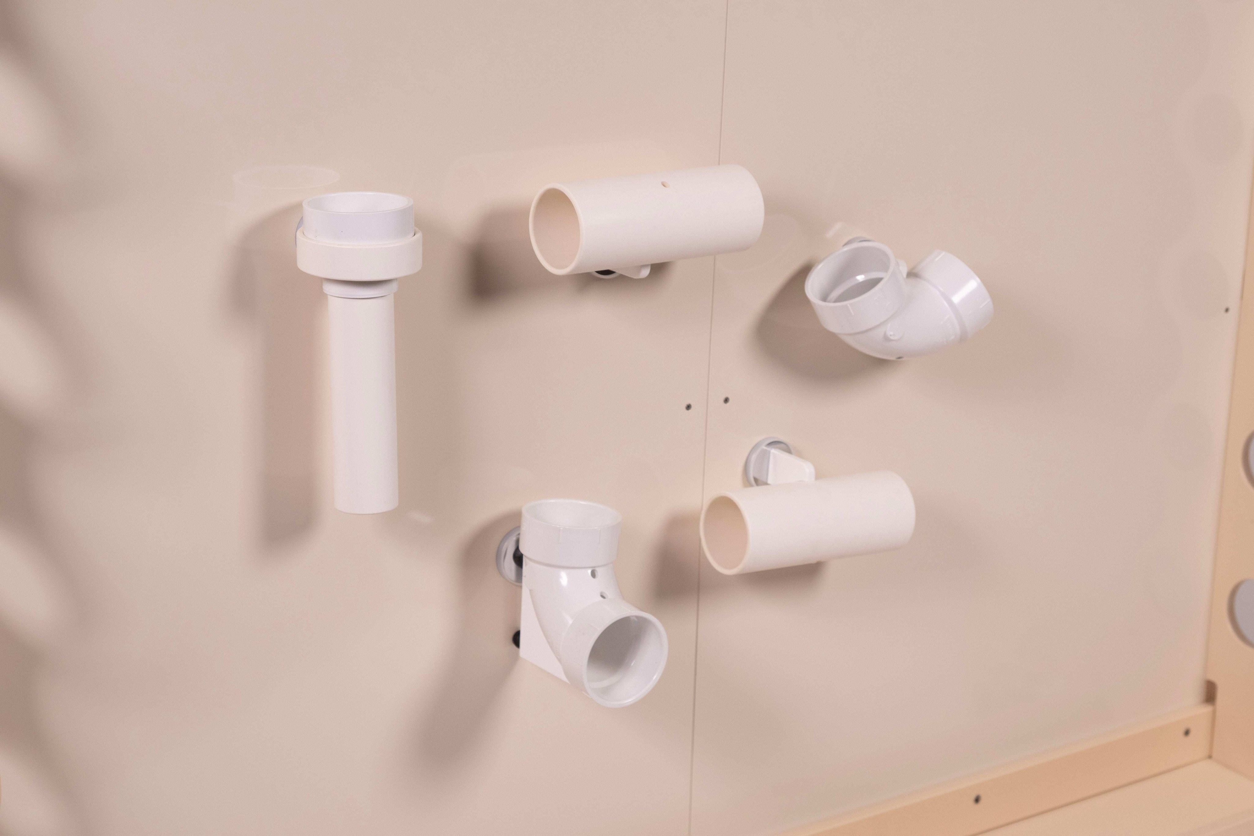 White plastic magnetic chutes and tubes attached to a smooth, light-colored wall for interactive play.