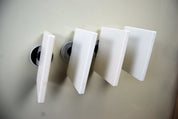 Four white square magnetic tiles attached to a smooth, light-colored wall surface.