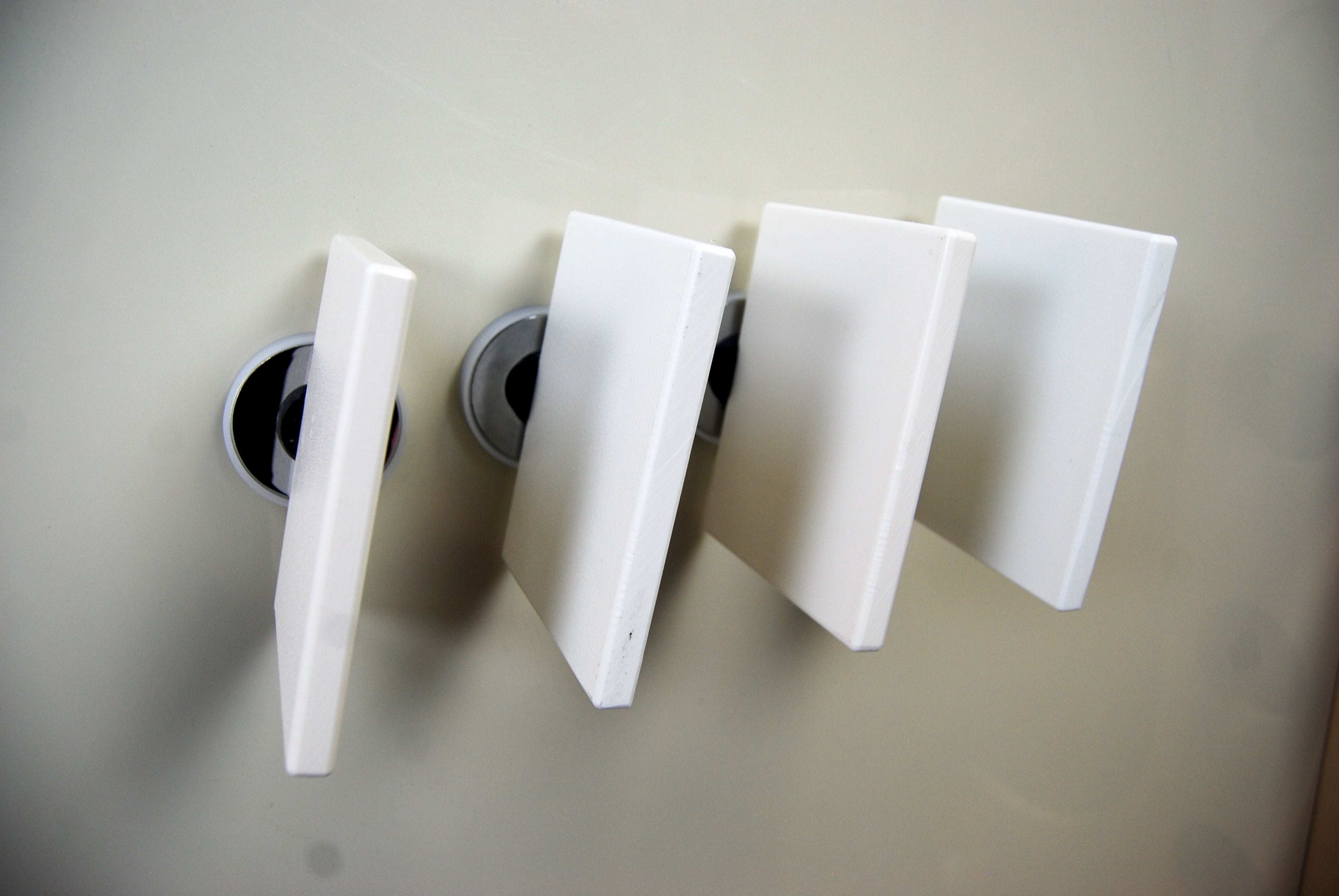 Four white square magnetic tiles attached to a smooth, light-colored wall surface.