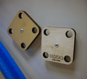 Two square wooden mounting platforms with four corner holes attached to a magnetic wall.