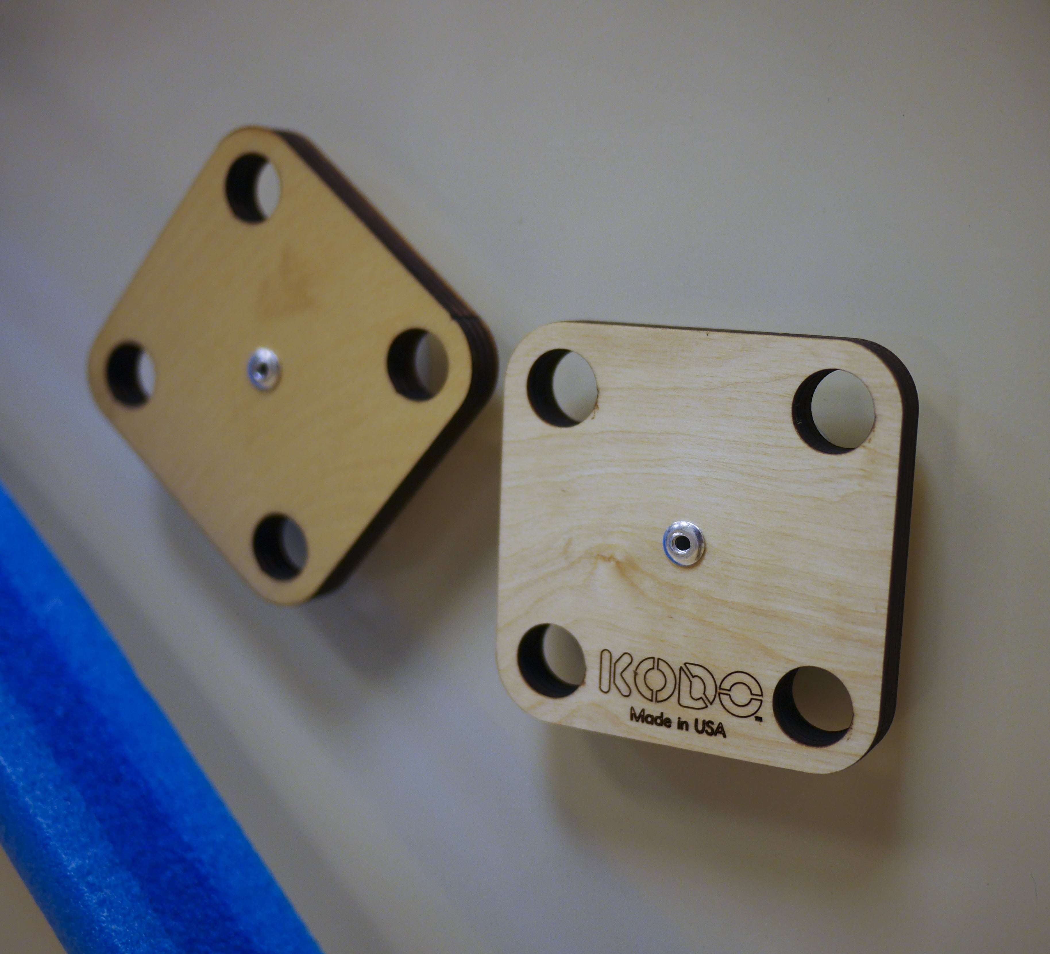 Two square wooden mounting platforms with four corner holes attached to a magnetic wall.