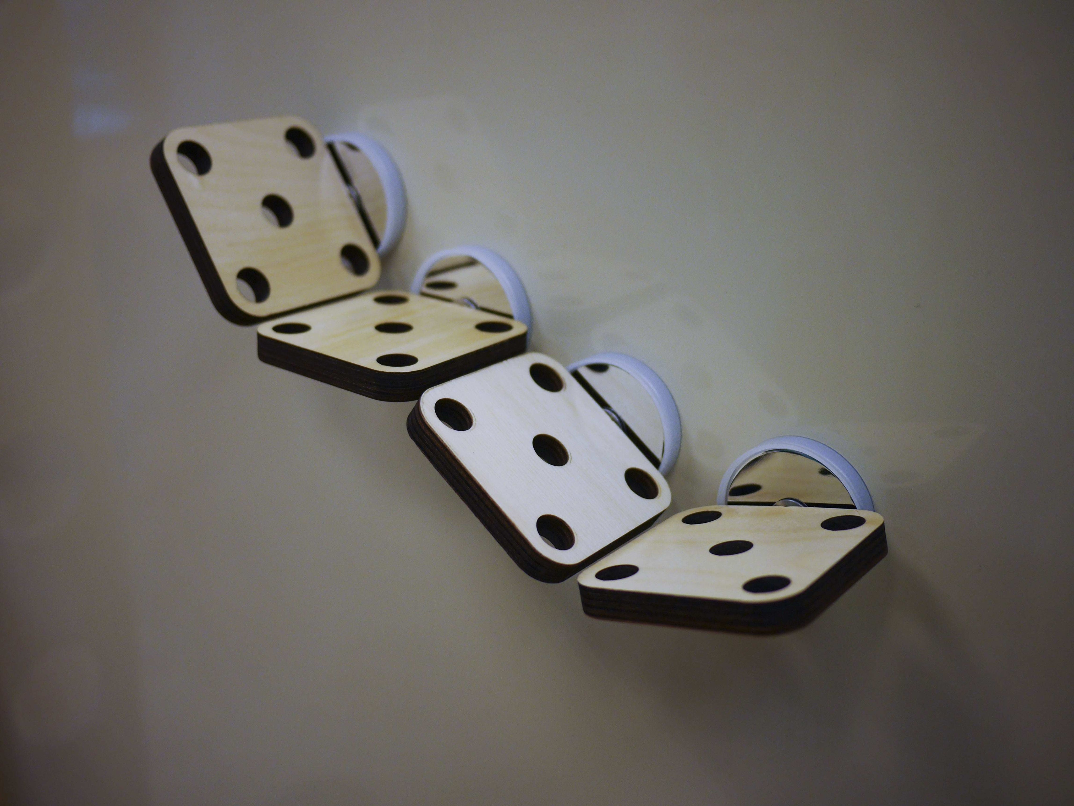 Four square, light-wood mounting platforms with circular holes attached to a magnetic surface with white clips.