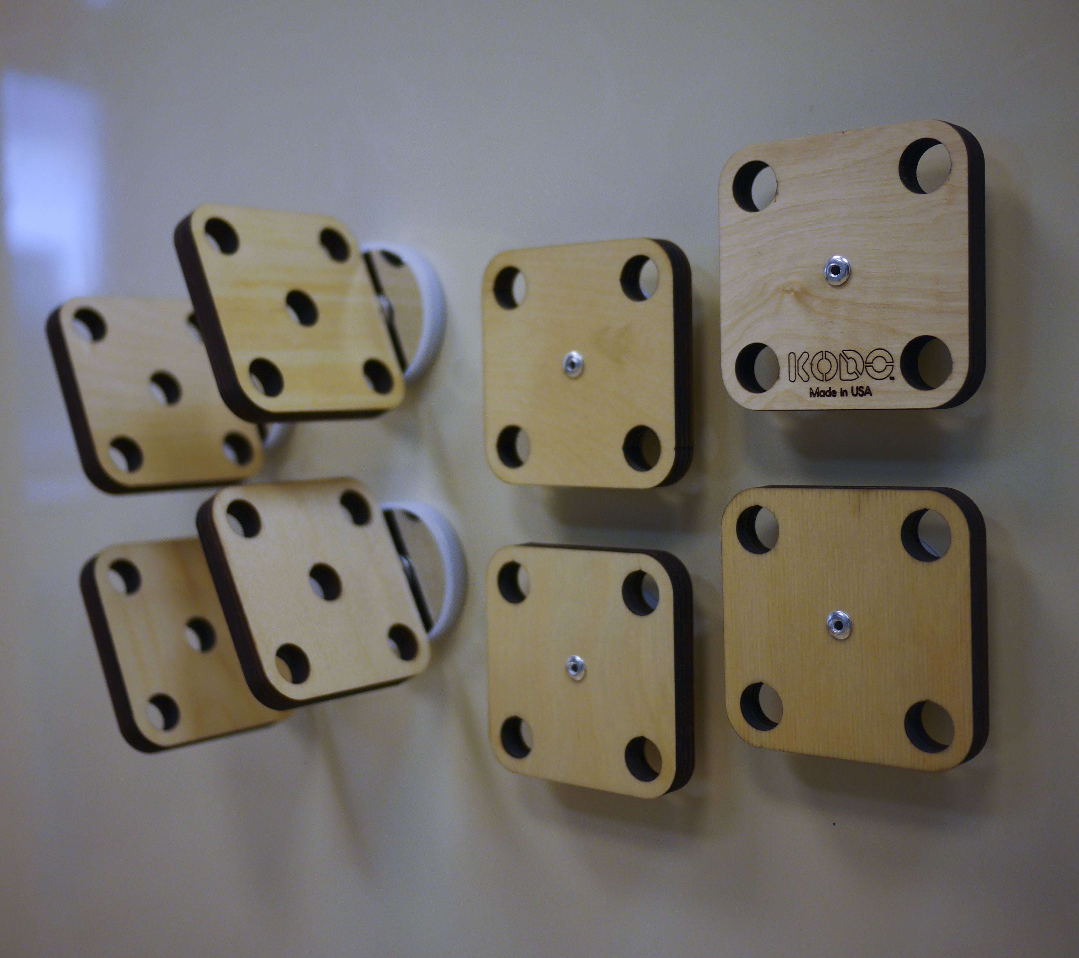 Eight square wooden mounting platforms with circular cutouts attached to a magnetic wall for engineering projects.