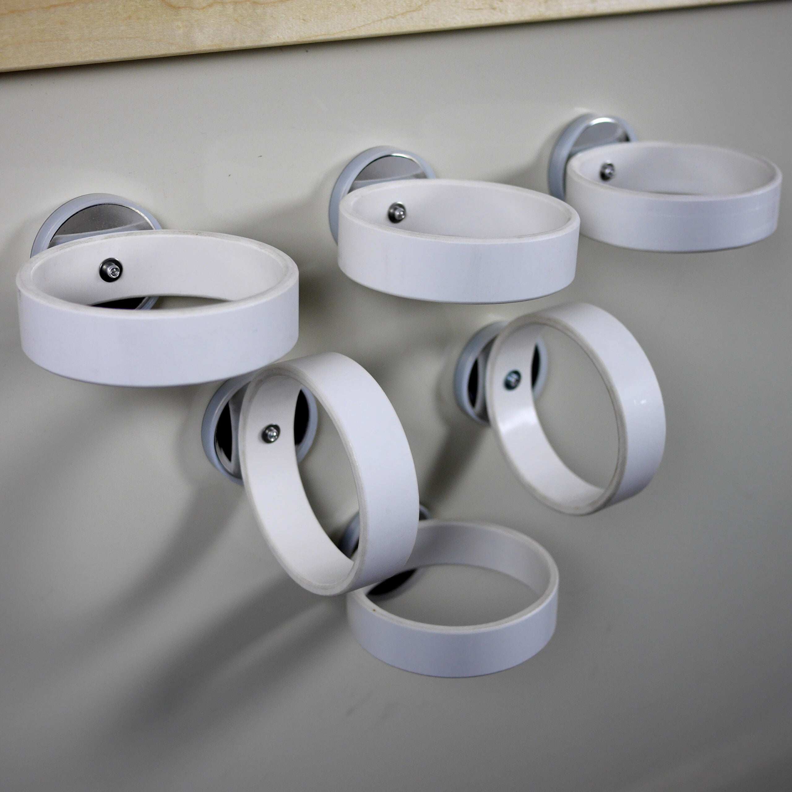 Six white magnetic rings with silver bases attached to a wall for holding ramps and materials.