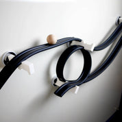Flexible black rubber ramp track with a wooden ball on a white magnetic wall, supported by white plastic pegs.
