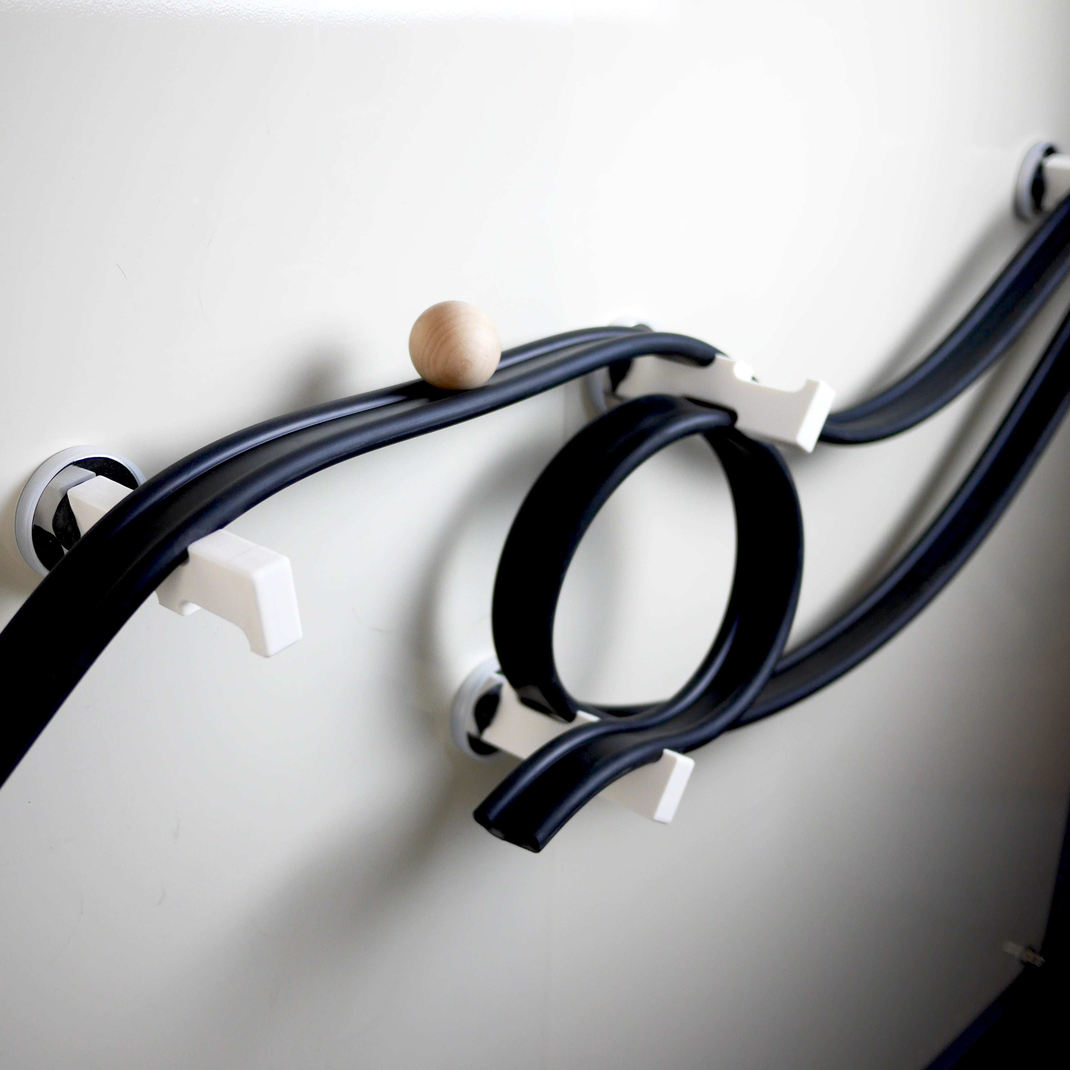 Flexible black rubber ramp track with a wooden ball on a white magnetic wall, supported by white plastic pegs.