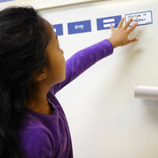 Child placing blue magnetic word and symbol tiles on a white classroom wall for educational ramp play.