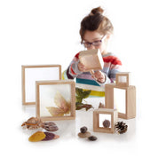 Child playing with six hardwood magnifying blocks featuring acrylic windows to examine nature items like leaves and shells.