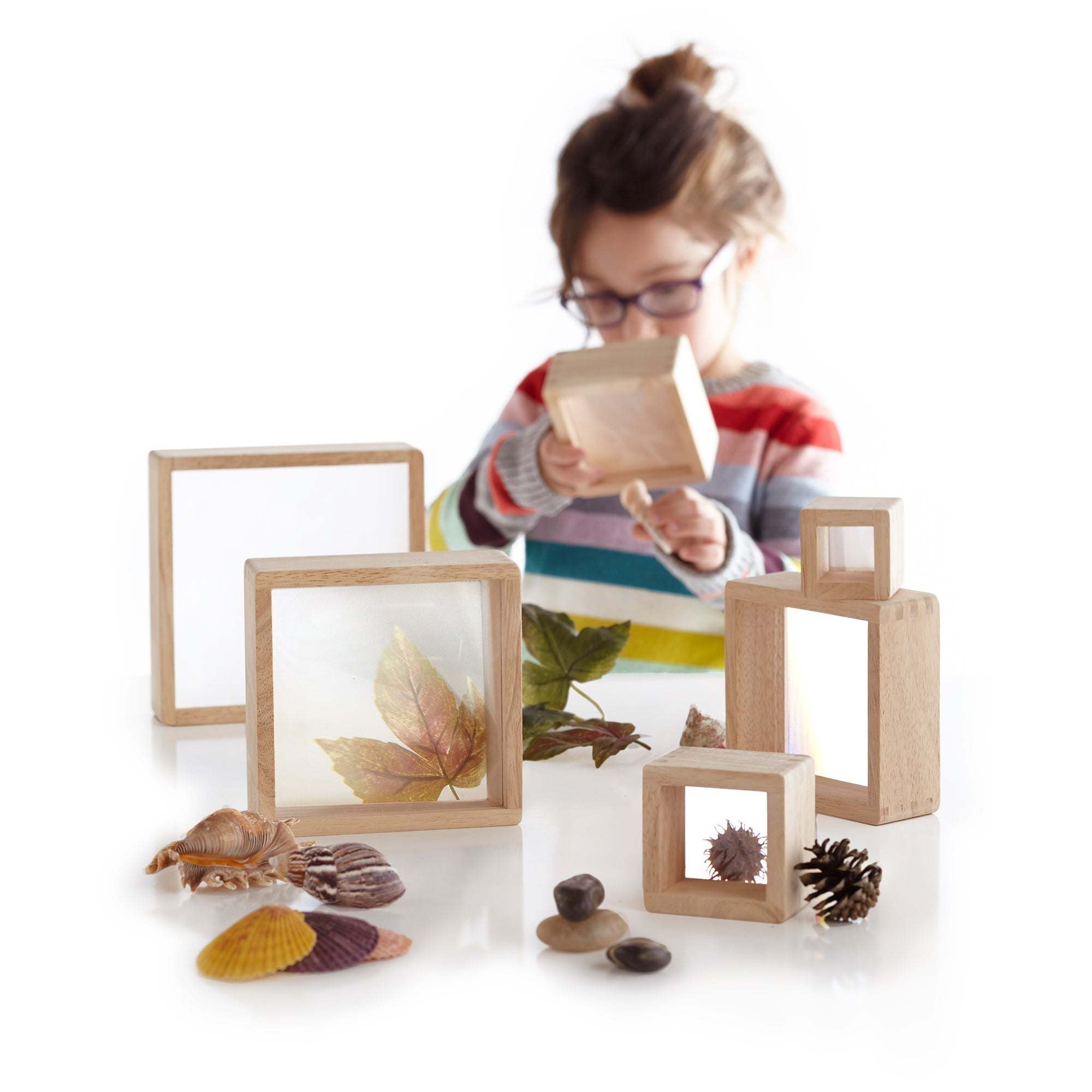 Child playing with six hardwood magnifying blocks featuring acrylic windows to examine nature items like leaves and shells.