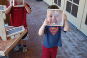 Child holding a square hardwood block with an inset magnifying acrylic lens to look through.