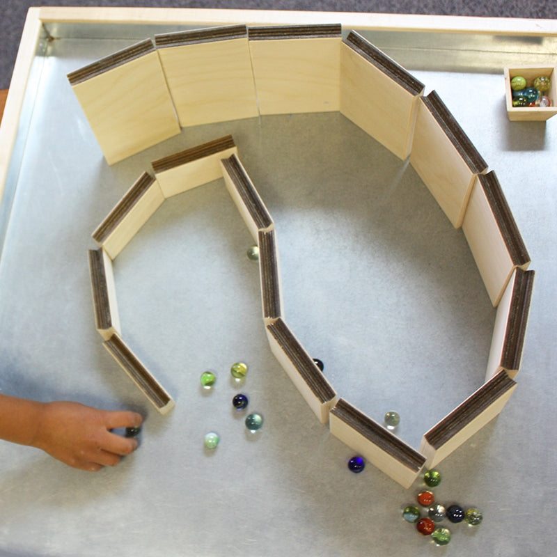 Child building a winding marble maze with light wood ramps and colorful glass marbles on a metal tray.