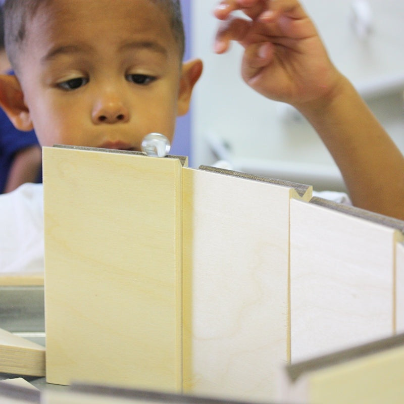 Child playing with light wood marble maze ramps and a clear glass marble.