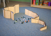Customizable wooden marble maze ramps arranged on a blue carpet with a collection of colorful glass marbles.